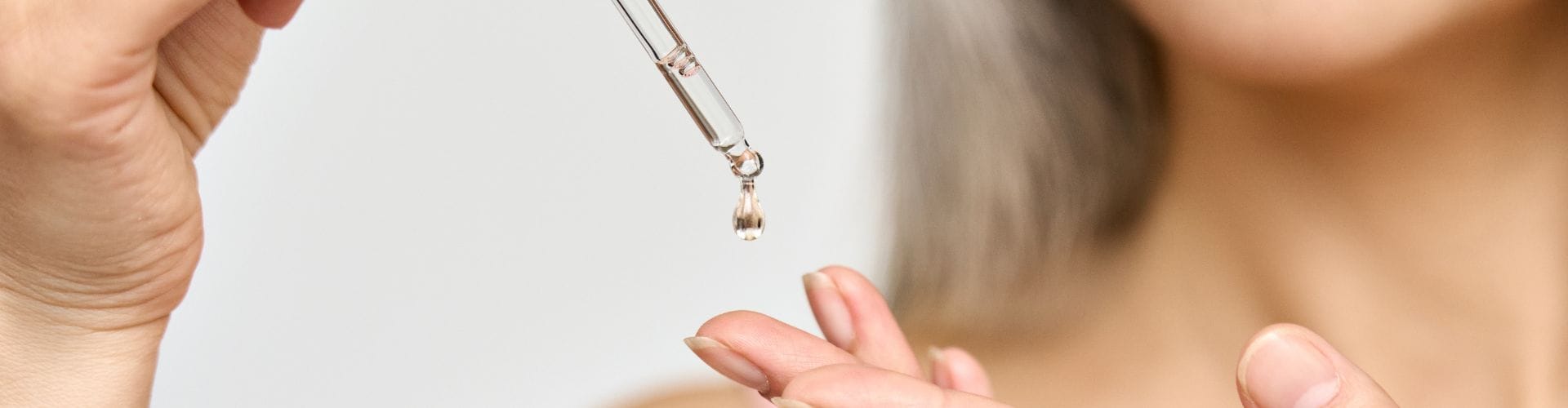 A close-up of a woman applying sunflower oil to her hand with a dropper, focusing on skincare application.