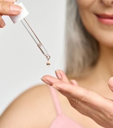 A close-up of a woman applying sunflower oil to her hand with a dropper, focusing on skincare application.