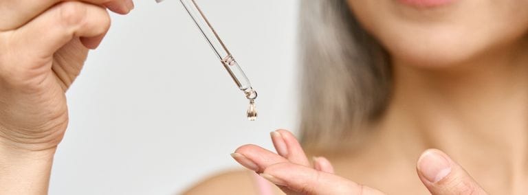 A close-up of a woman applying sunflower oil to her hand with a dropper, focusing on skincare application.