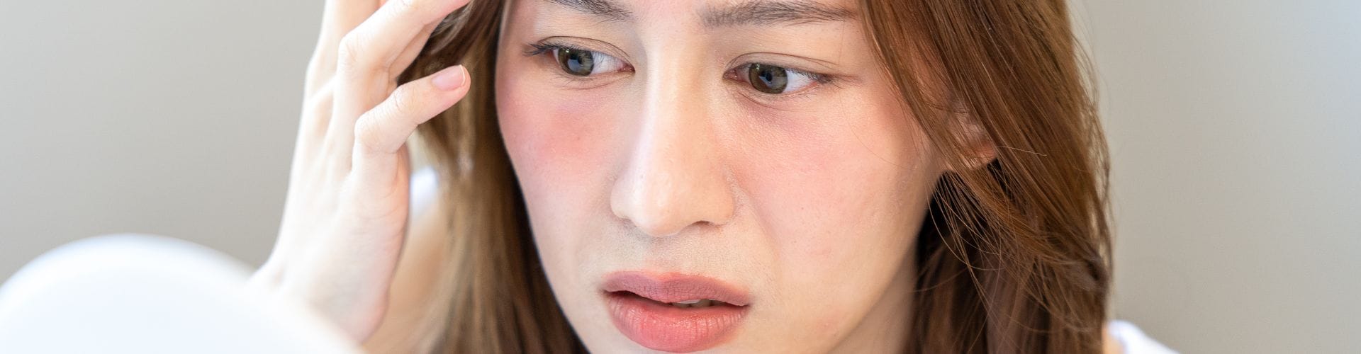 A concerned woman examining redness on her face, exploring the effects of formaldehyde on skin​.