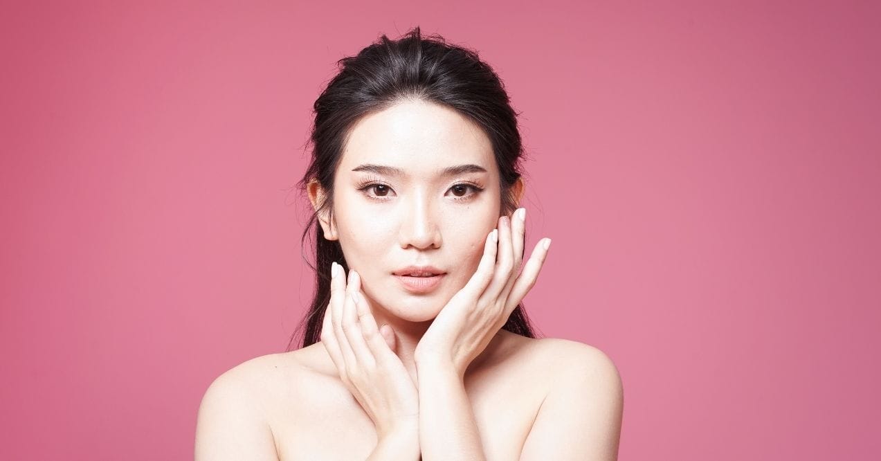 Woman with radiant skin posing against a pink background