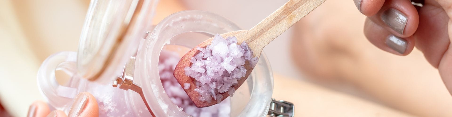 A close-up of purple bath salt being scooped, answering the question, is salt water good for your skin.