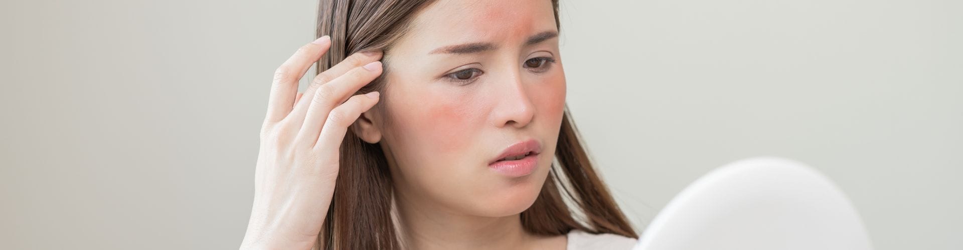 Concerned woman with skin irritation examining her face in a mirror.