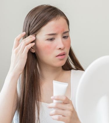 Concerned woman with skin irritation examining her face in a mirror.