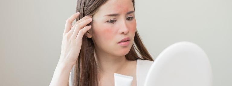 Concerned woman with skin irritation examining her face in a mirror.