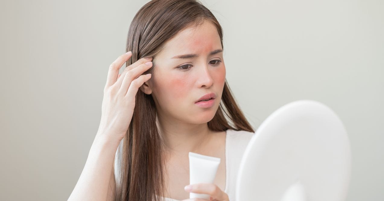 Concerned woman with skin irritation examining her face in a mirror.