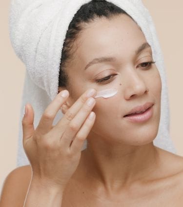 Woman applying moisturizer under her eye, promoting smooth and hydrated skin.