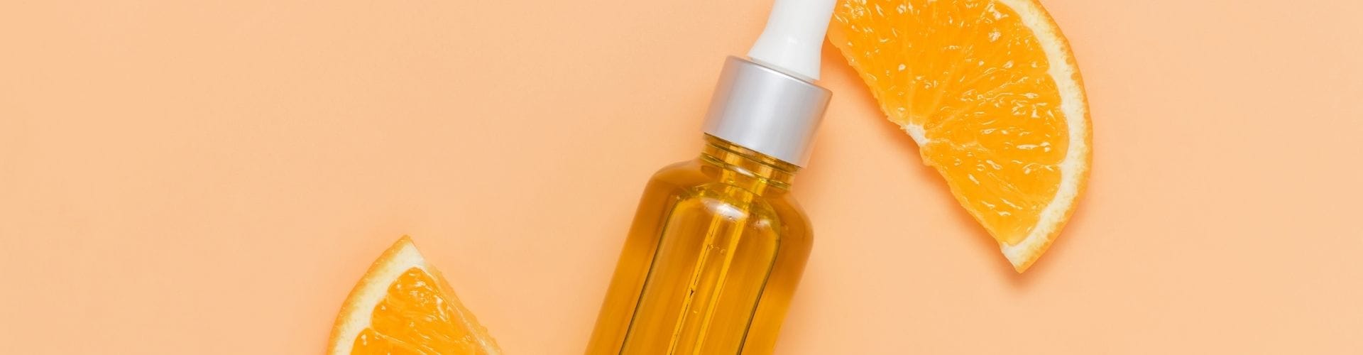 Vitamin C serum bottle with fresh orange slices on a peach background