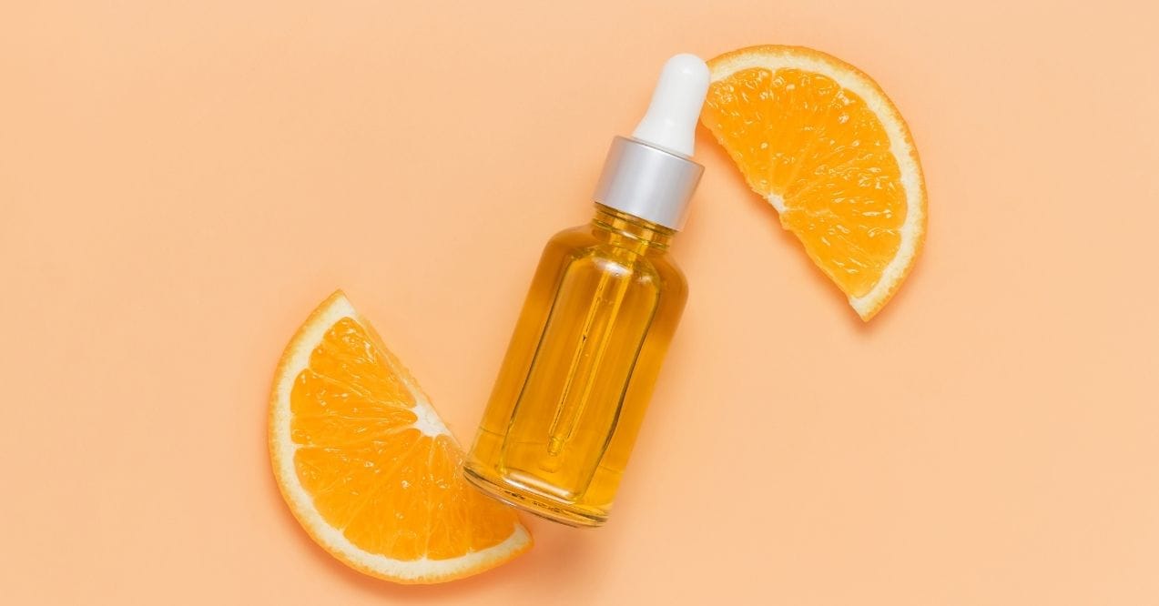 Vitamin C serum bottle with fresh orange slices on a peach background