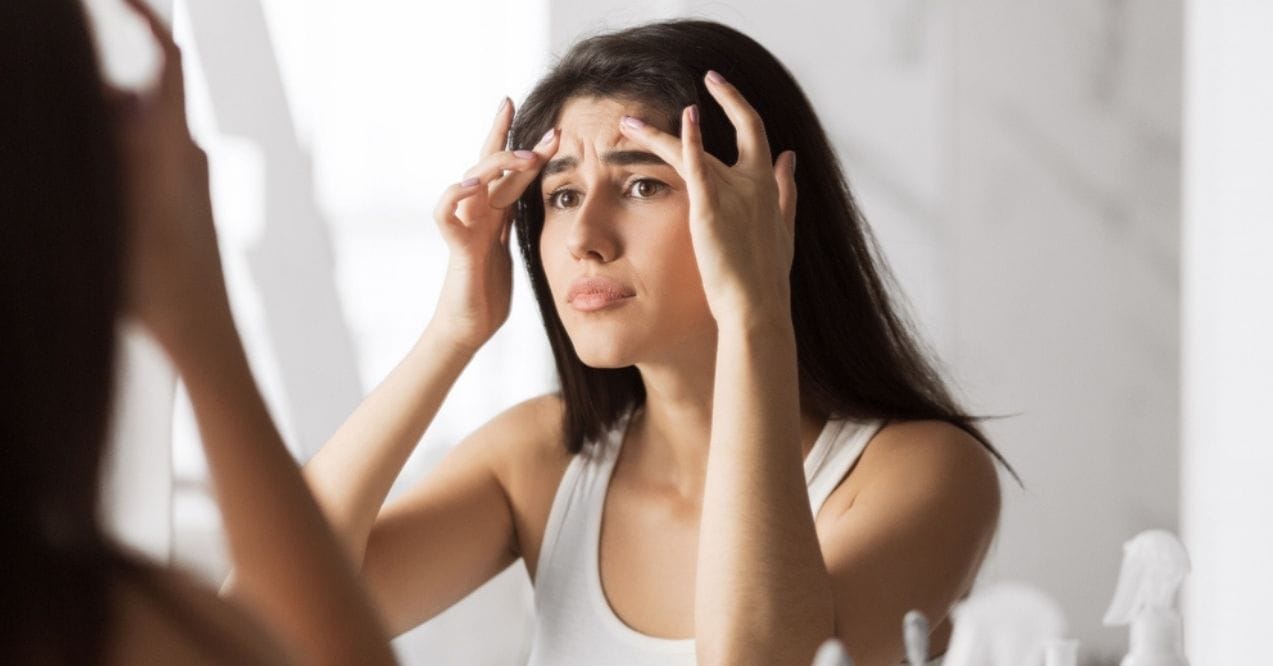 Woman examining forehead wrinkles in the mirror