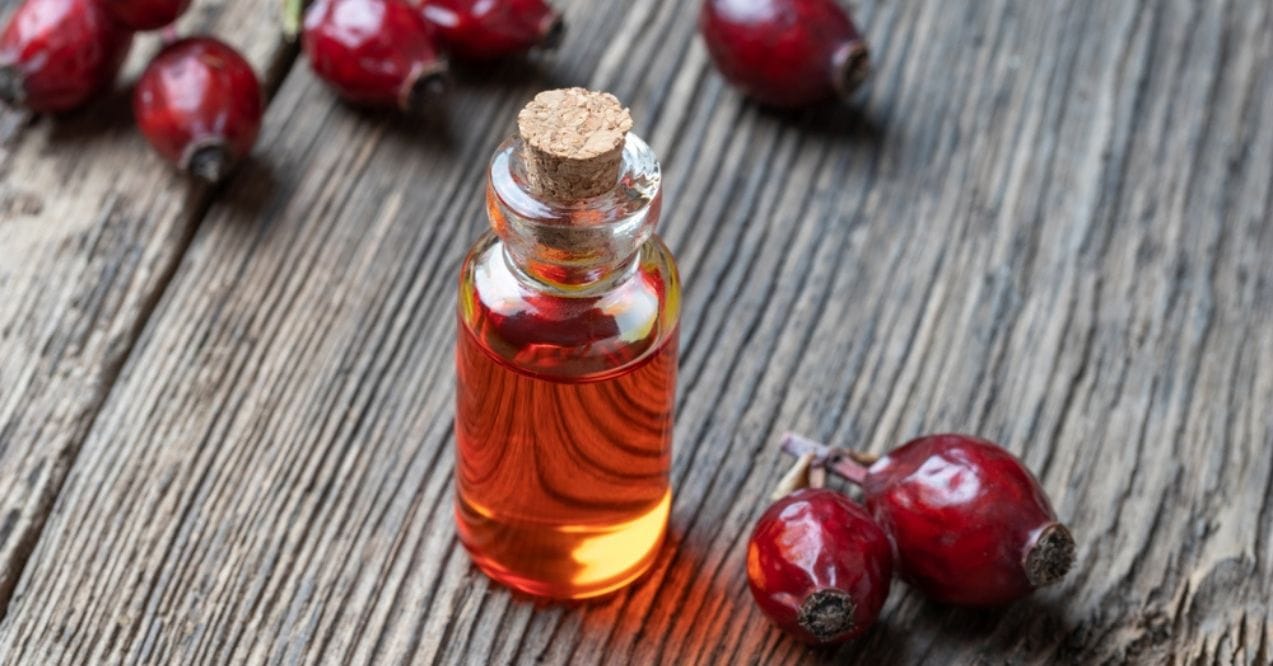 Small glass bottle of rosehip oil with fresh rosehips on a rustic wooden surface