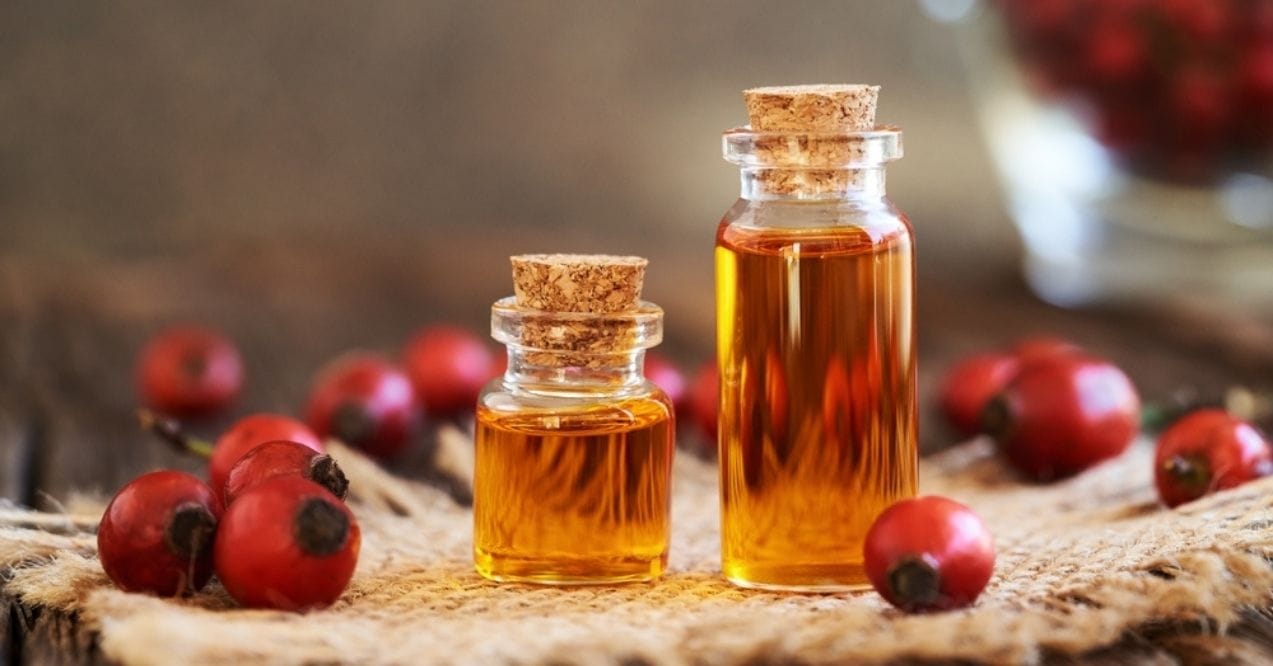 Bottles of golden rosehip oil with fresh rosehips on a rustic wooden surface