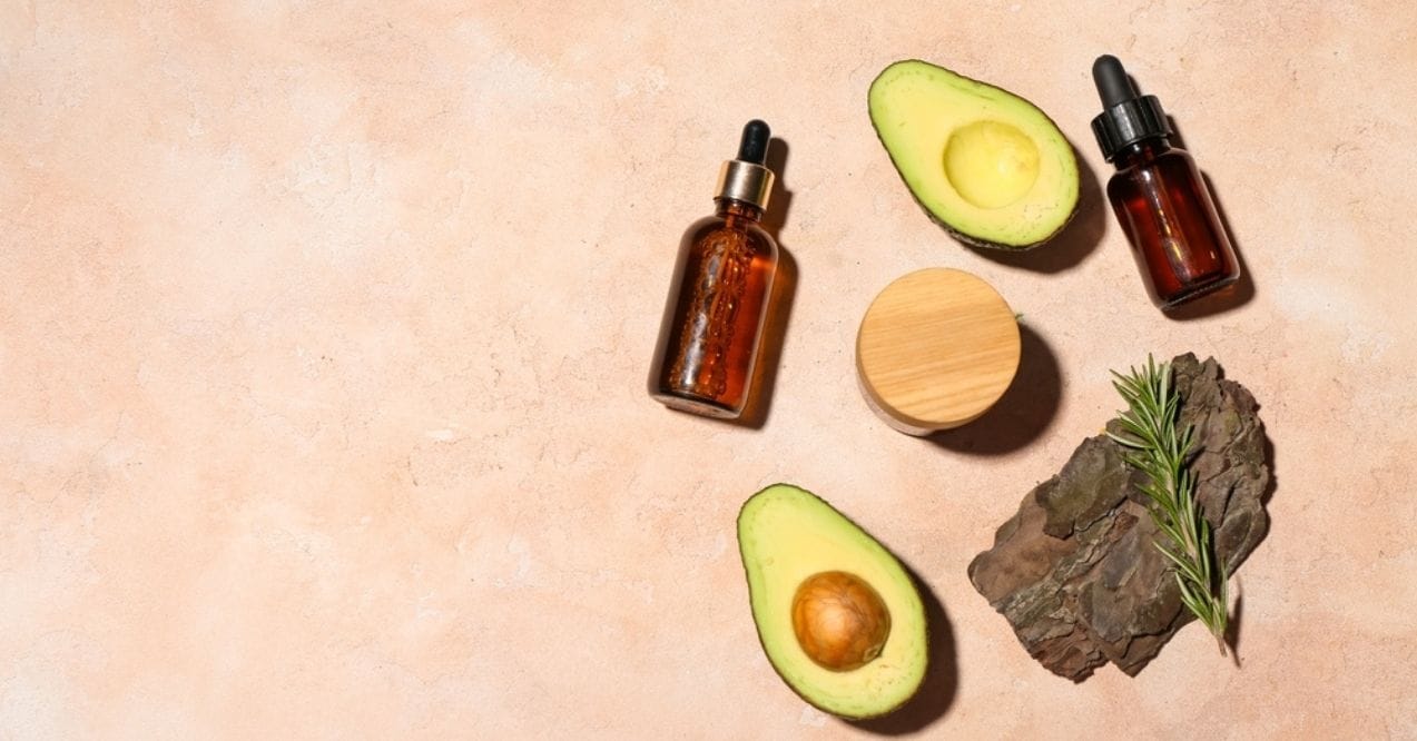 Avocado oil bottles with fresh avocados on a beige background