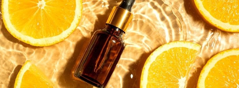 A dropper bottle of serum surrounded by fresh orange slices