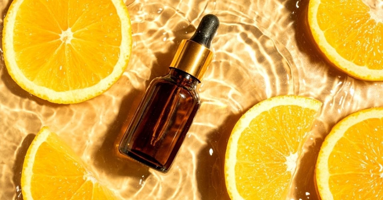 A dropper bottle of serum surrounded by fresh orange slices