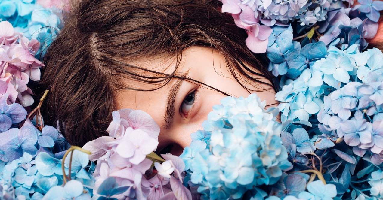 Young woman in a blue beret posing among pink spring blossoms