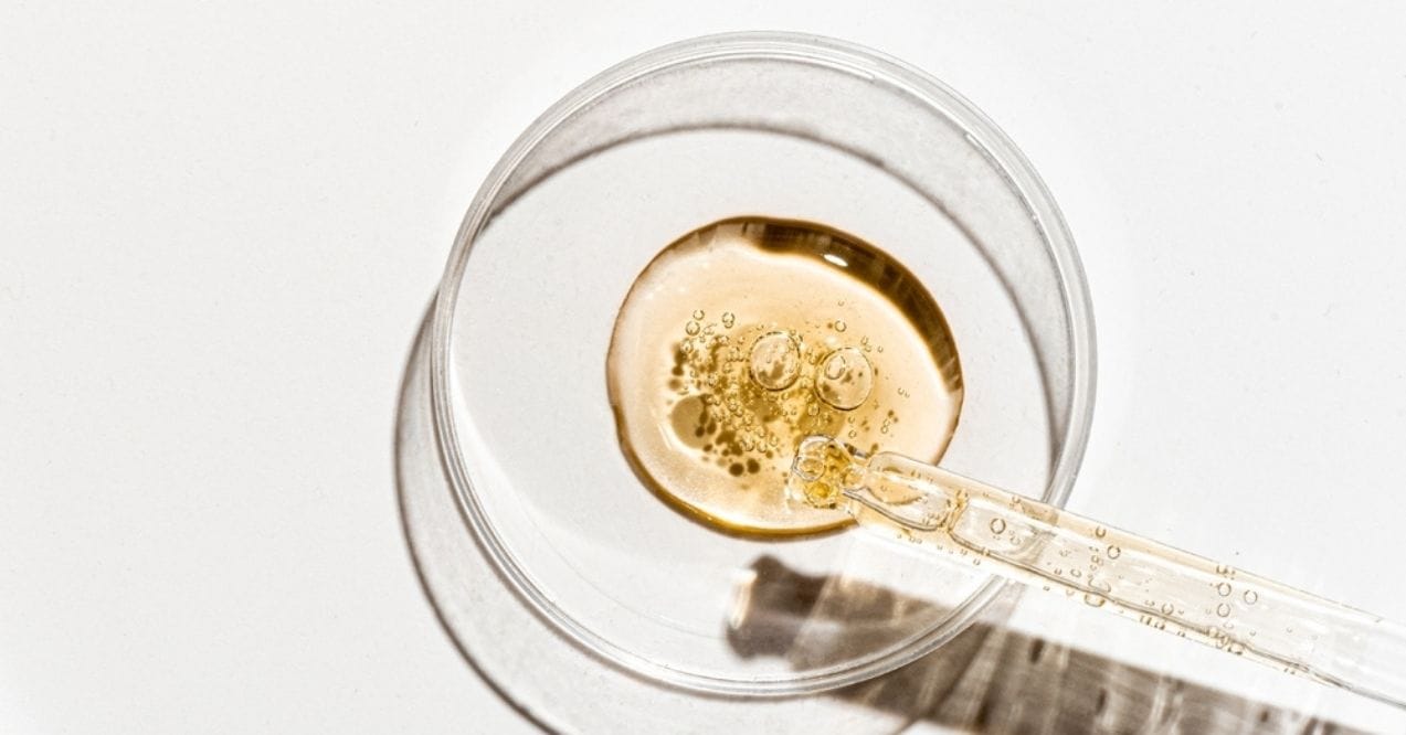 Close-up of a dropper releasing serum into a glass petri dish