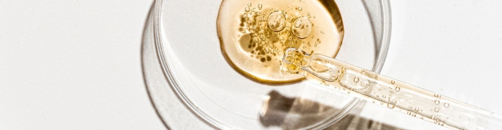 Close-up of a dropper releasing serum into a glass petri dish