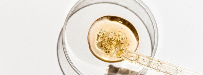 Close-up of a dropper releasing serum into a glass petri dish