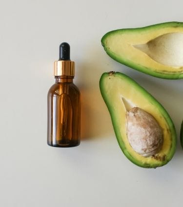 Brown dropper bottle with halved avocados on a white surface