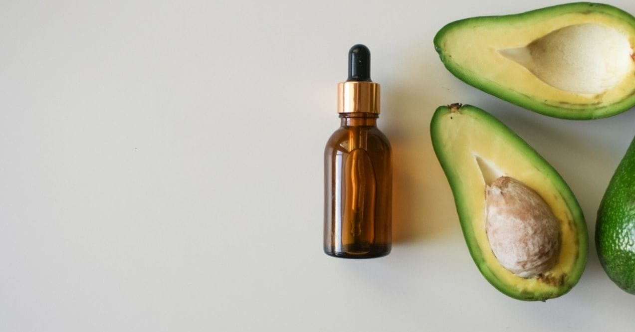 Brown dropper bottle with halved avocados on a white surface