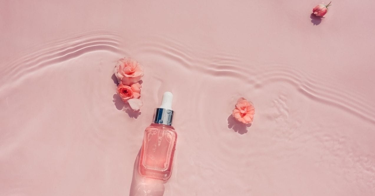 Pink serum bottle with flowers floating in water