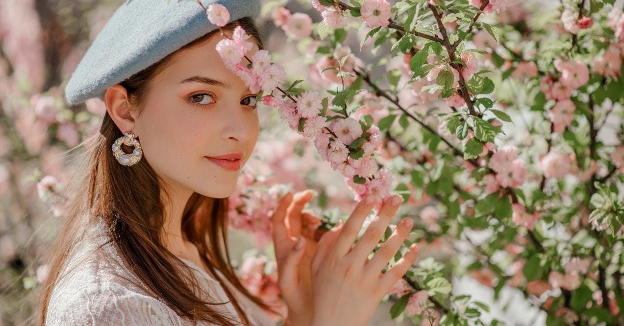 Young woman in a blue beret posing among pink spring blossoms