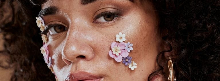 Close-up of a woman with glowing skin and small pastel flowers on her face