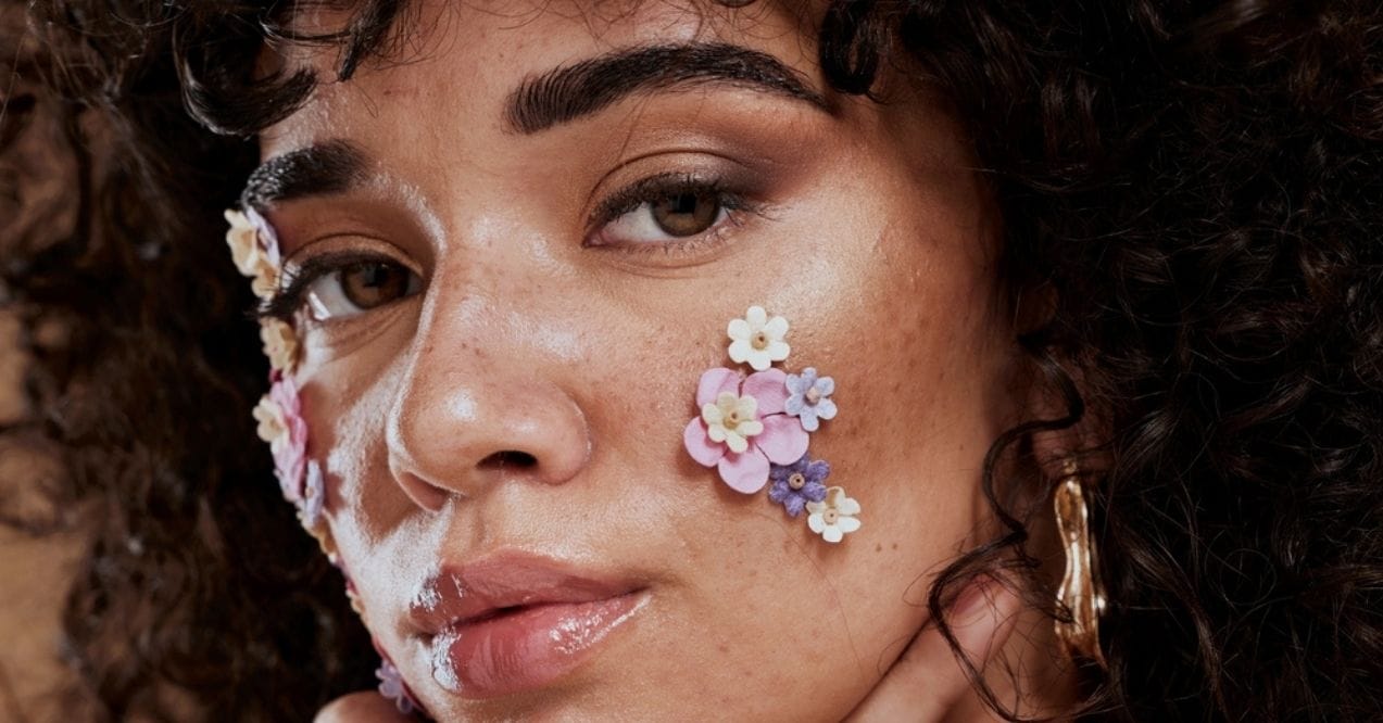 Close-up of a woman with glowing skin and small pastel flowers on her face