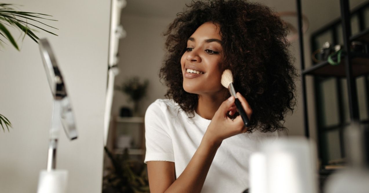 Smiling woman applying makeup in front of a mirror