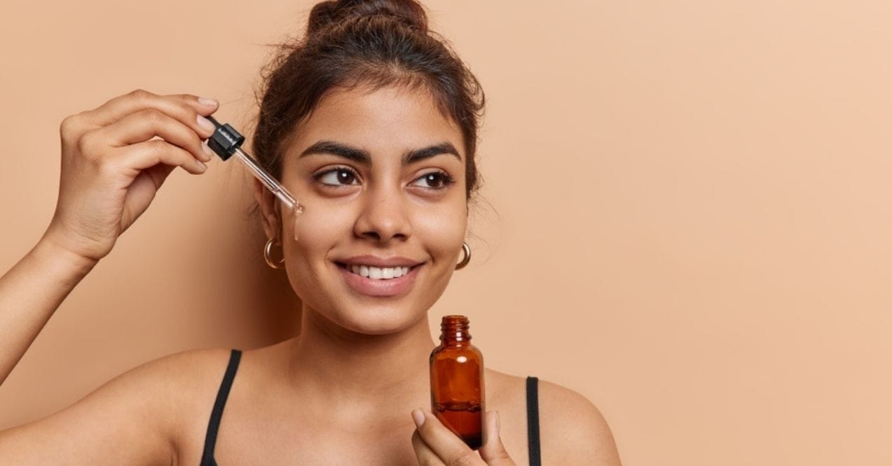 Smiling woman applying serum to her face with a dropper