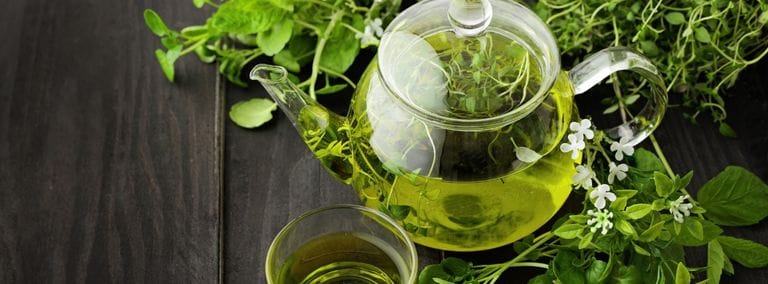 Glass teapot with green herbal tea and fresh herbs