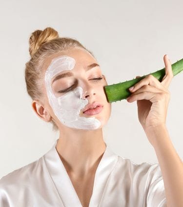 Woman applying aloe vera leaf to her face with a cream mask on