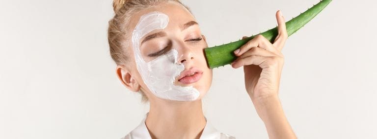 Woman applying aloe vera leaf to her face with a cream mask on