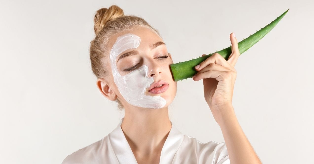 Woman applying aloe vera leaf to her face with a cream mask on