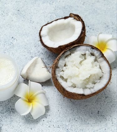 Open coconuts, coconut pieces, white jar of coconut cream, and white flowers arranged
