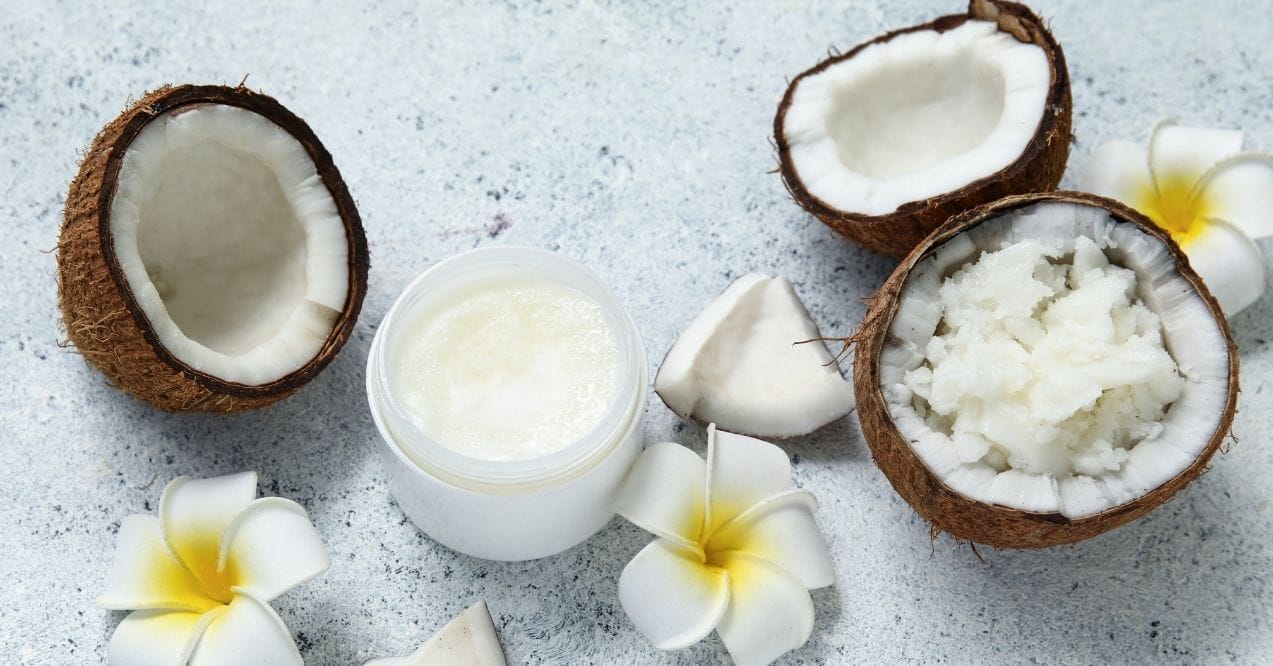 Open coconuts, coconut pieces, white jar of coconut cream, and white flowers arranged