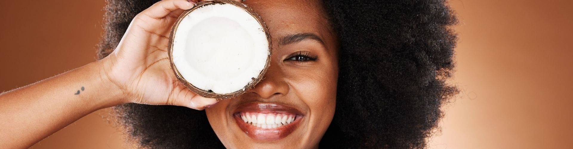Smiling woman holding two halves of a coconut near her face