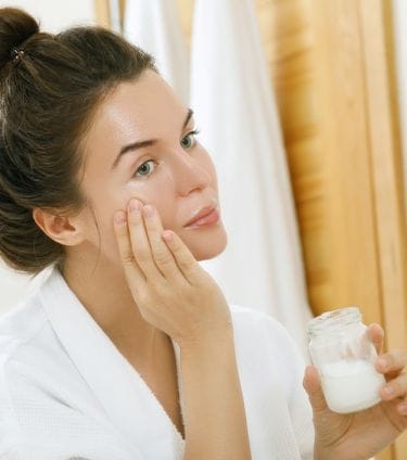 Woman applying coconut oil to her face in front of mirror