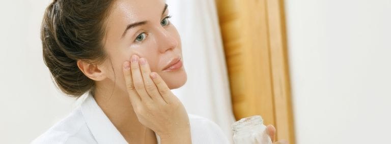Woman applying coconut oil to her face in front of mirror