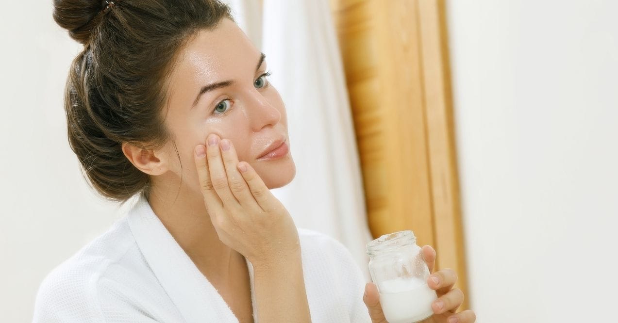 Woman applying coconut oil to her face in front of mirror