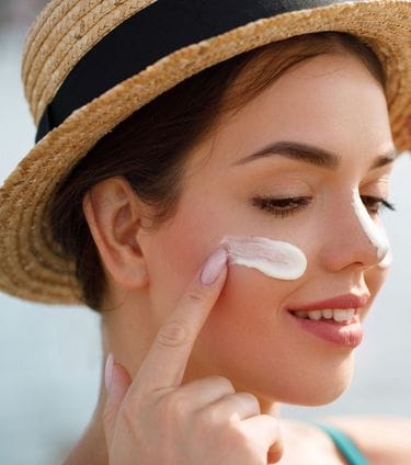 Woman applying sunscreen to her face while wearing a straw hat