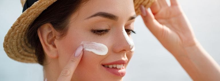 Woman applying sunscreen to her face while wearing a straw hat