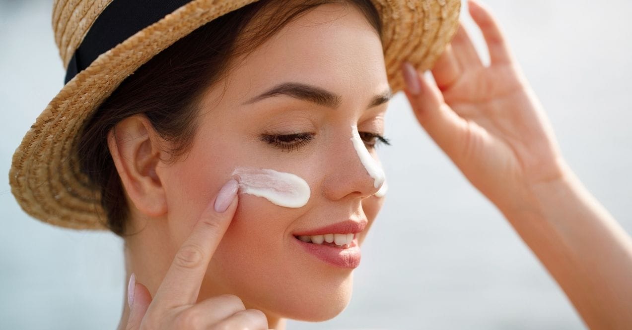 Woman applying sunscreen to her face while wearing a straw hat