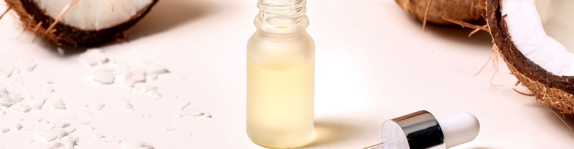 Coconut oil in dropper bottle surrounded by halved coconuts