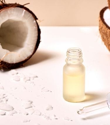 Coconut oil in dropper bottle surrounded by halved coconuts