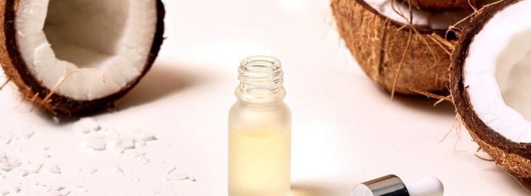 Coconut oil in dropper bottle surrounded by halved coconuts