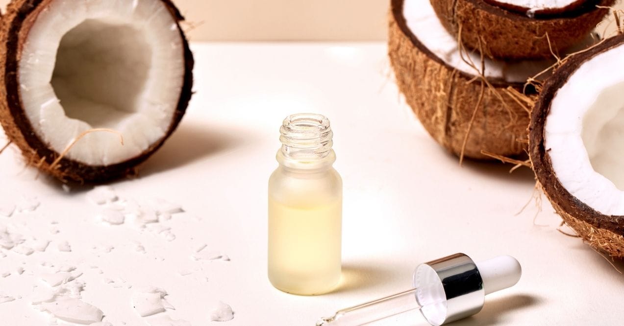 Coconut oil in dropper bottle surrounded by halved coconuts