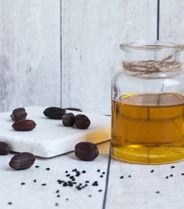Glass jar of golden jojoba oil with scattered jojoba seeds