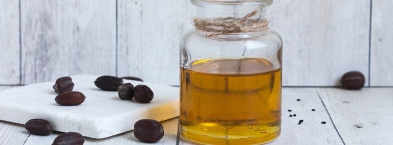 Glass jar of golden jojoba oil with scattered jojoba seeds
